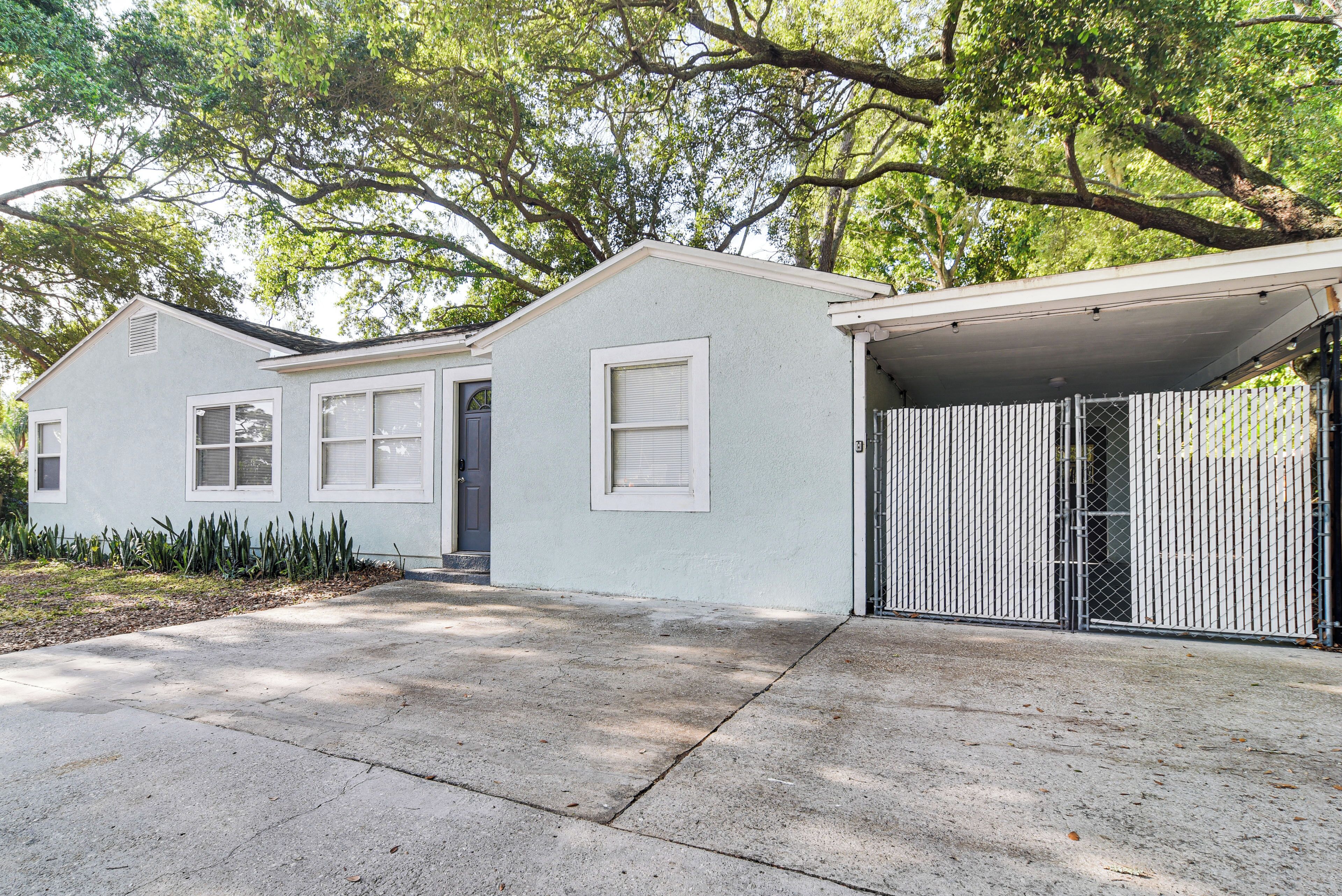 A single-story house with a garage, a covered driveway, and a small front yard with plants.