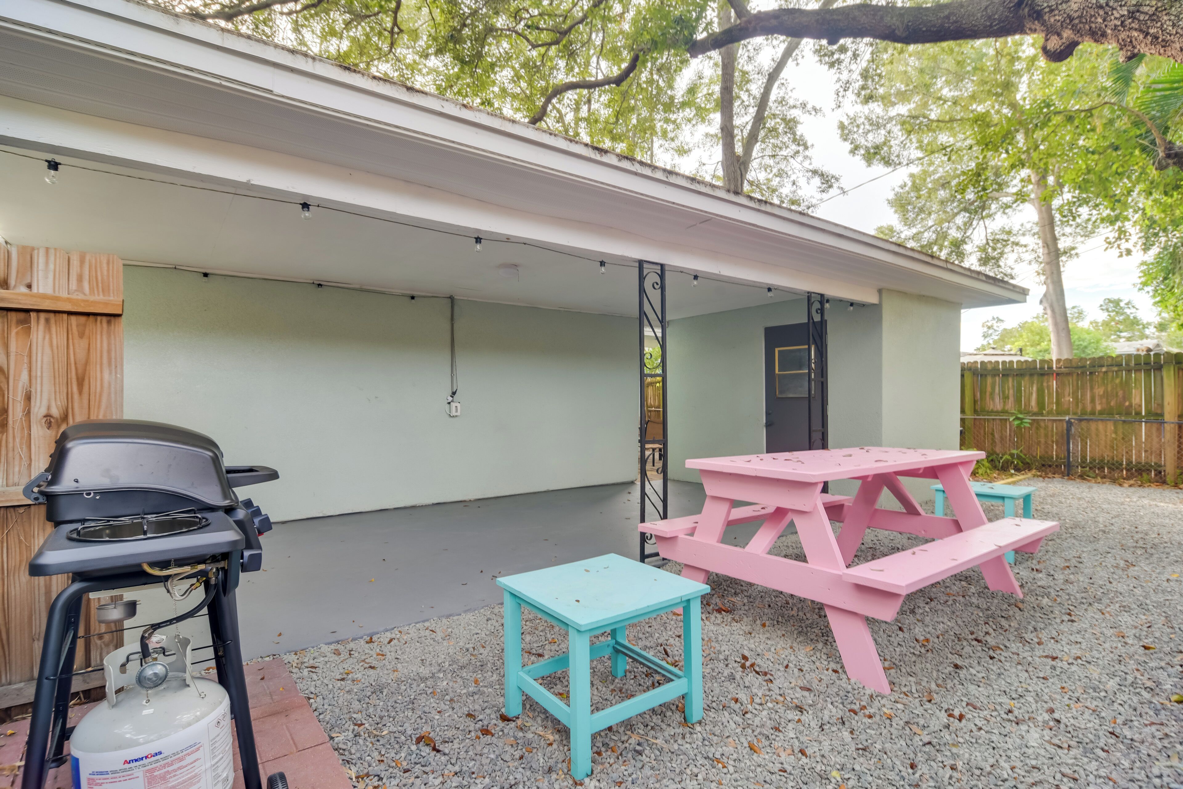 Un patio techado con una parrilla, una mesa de picnic y un taburete pequeño.