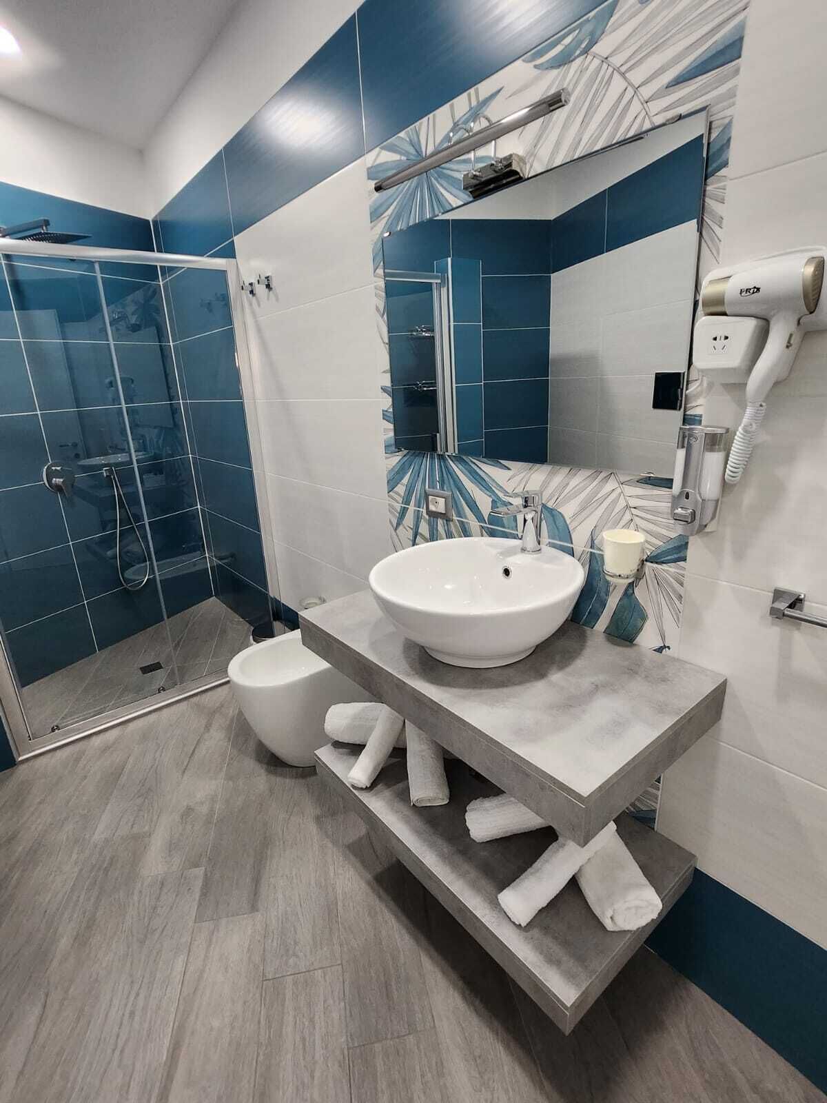 A modern bathroom with a glass shower enclosure, a white sink, and a hairdryer mounted on the wall.