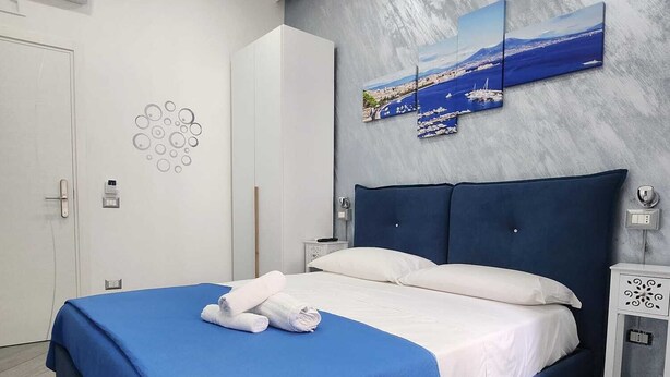 A modern bedroom with a large bed, a view of the sea, and a grey textured wall. - GRADINI PARTENOPEI (Naples)