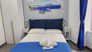 A modern hotel room with a large bed, a headboard with a cityscape painting, a wardrobe, and a blue curtain. - GRADINI PARTENOPEI (Naples)