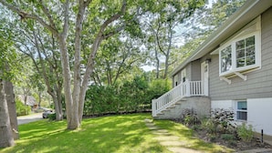 A residential property with a well-maintained lawn, a stone pathway leading to the front door, and mature trees providing shade. - Hampton Bays Retreat: Walk to Squires Beach! (Hampton Bays)
