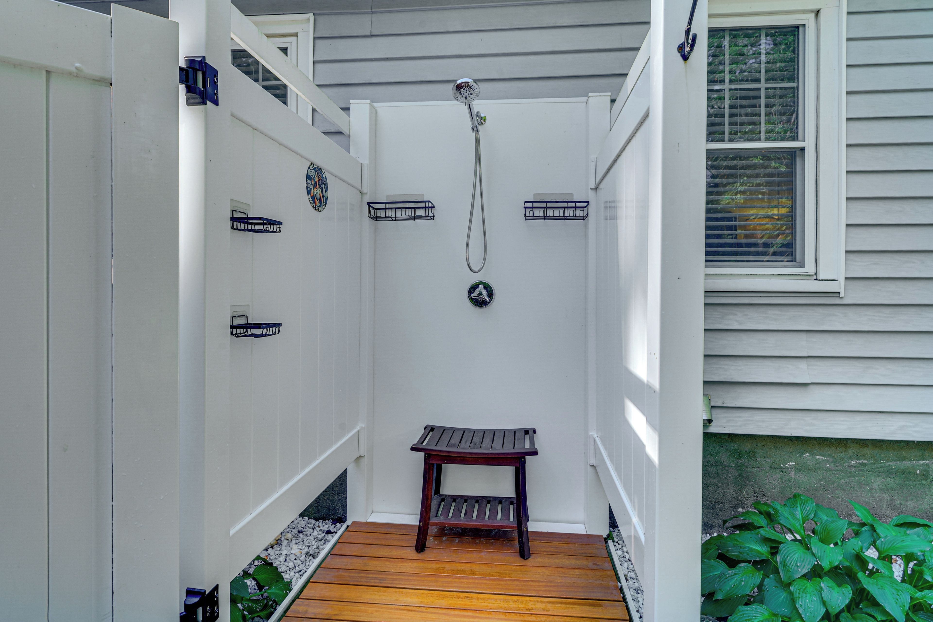 A covered outdoor shower area with a wooden bench, a hose, and a showerhead.