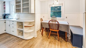 A kitchen with white cabinetry, a dining table with chairs, and a window with a view of trees. - Near Beach: Coastal Maine Getaway w/ Yard (Wells)