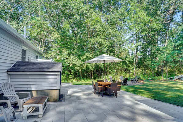 A patio with a table and chairs, a wooden bench, and an umbrella. - Near Beach: Coastal Maine Getaway w/ Yard (Wells)