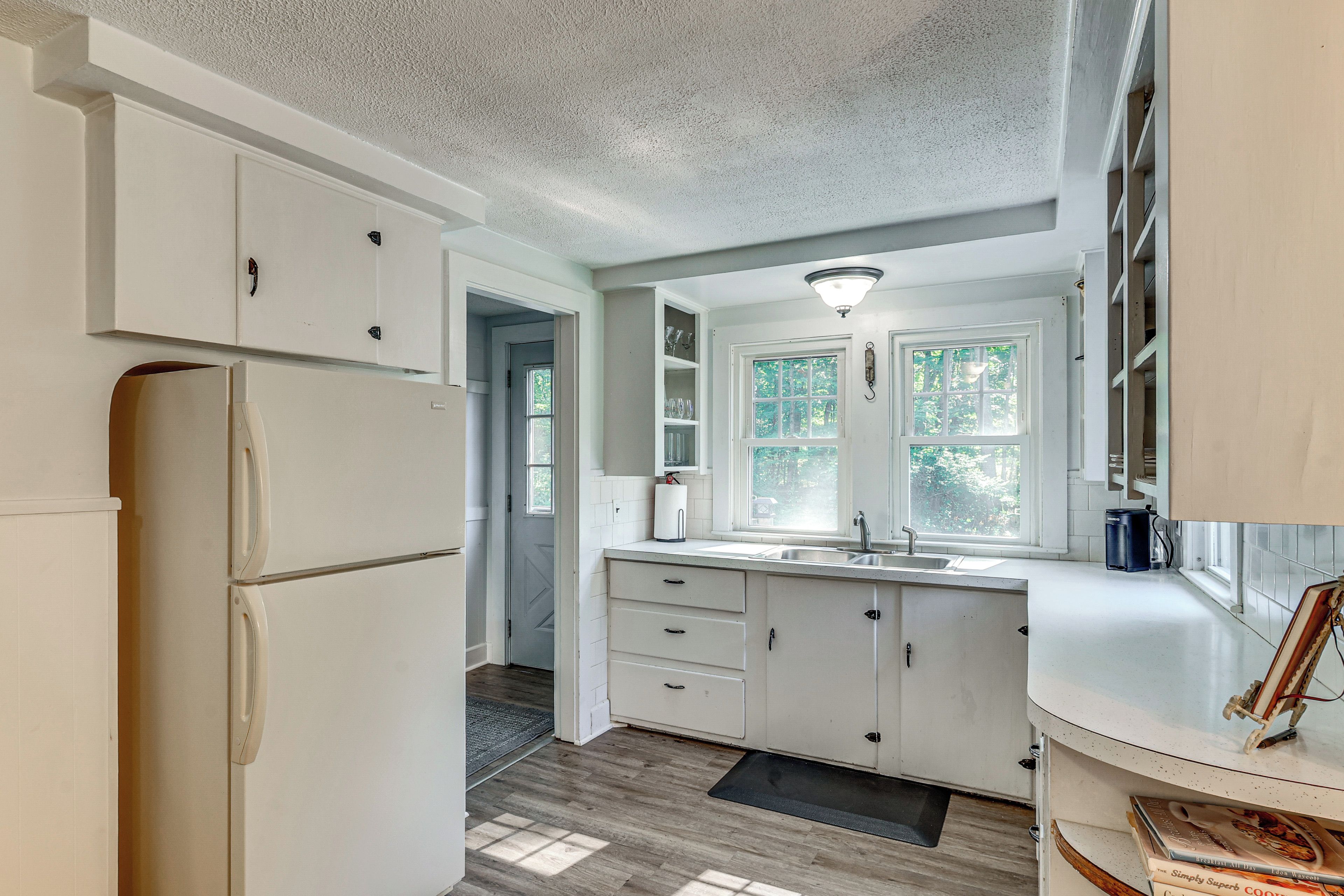 A kitchen with white cabinets, a refrigerator, a sink, and a window.