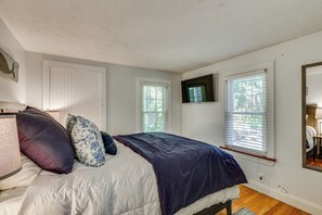 A bedroom with a bed, pillows, a flat-screen TV, and windows.