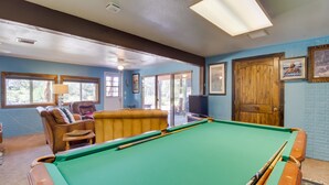 A pool table with cues, a leather chair, a sofa, and a television in a room with blue walls and wooden accents. - Peaceful Pinetop-lakeside Suite w/ Fire Pit! (Lakeside)