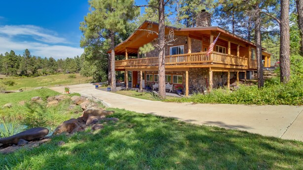 A two-story log cabin with a balcony, surrounded by trees and a small pond. - Peaceful Pinetop-lakeside Suite w/ Fire Pit! (Lakeside)