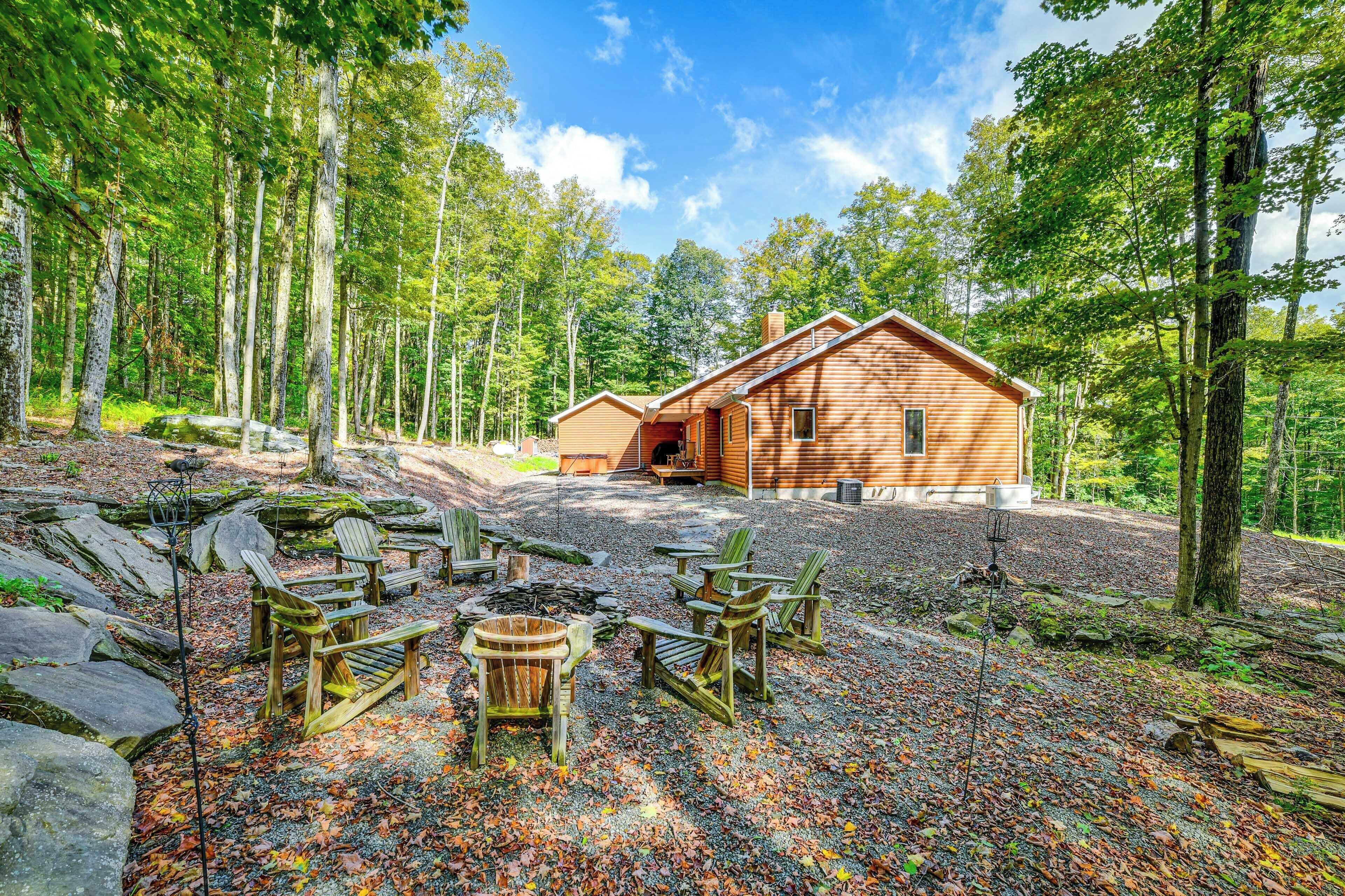 Eine Hütte mit einer terrasse aus Steinplatten, Holz-Adirondack-Stühlen und einer Feuerstelle.