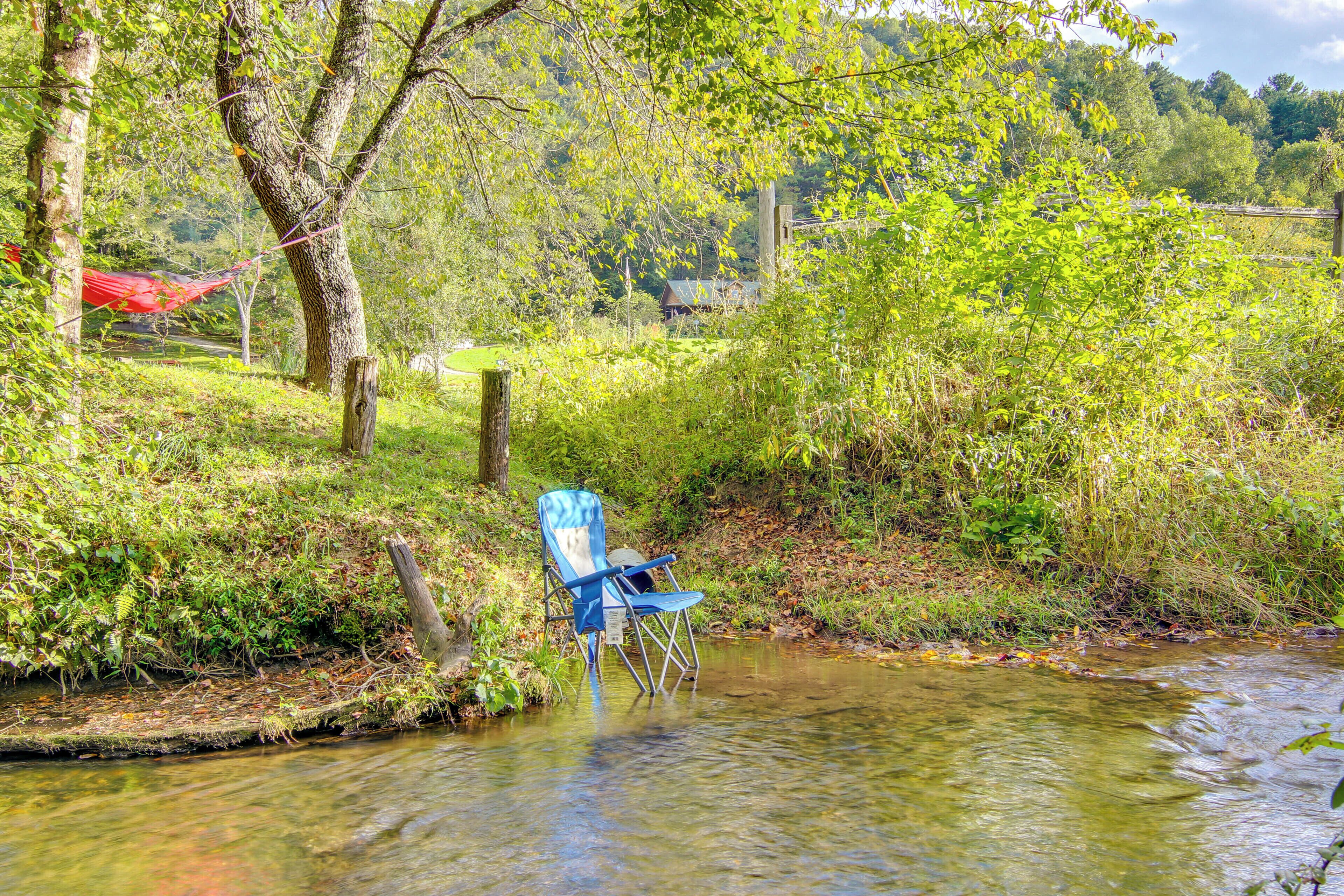A blue folding chair partially submerged in a clear stream, surrounded by lush greenery and trees.
