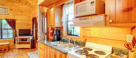 A wooden cabin kitchen with a stove, microwave, sink, and wooden cabinets.