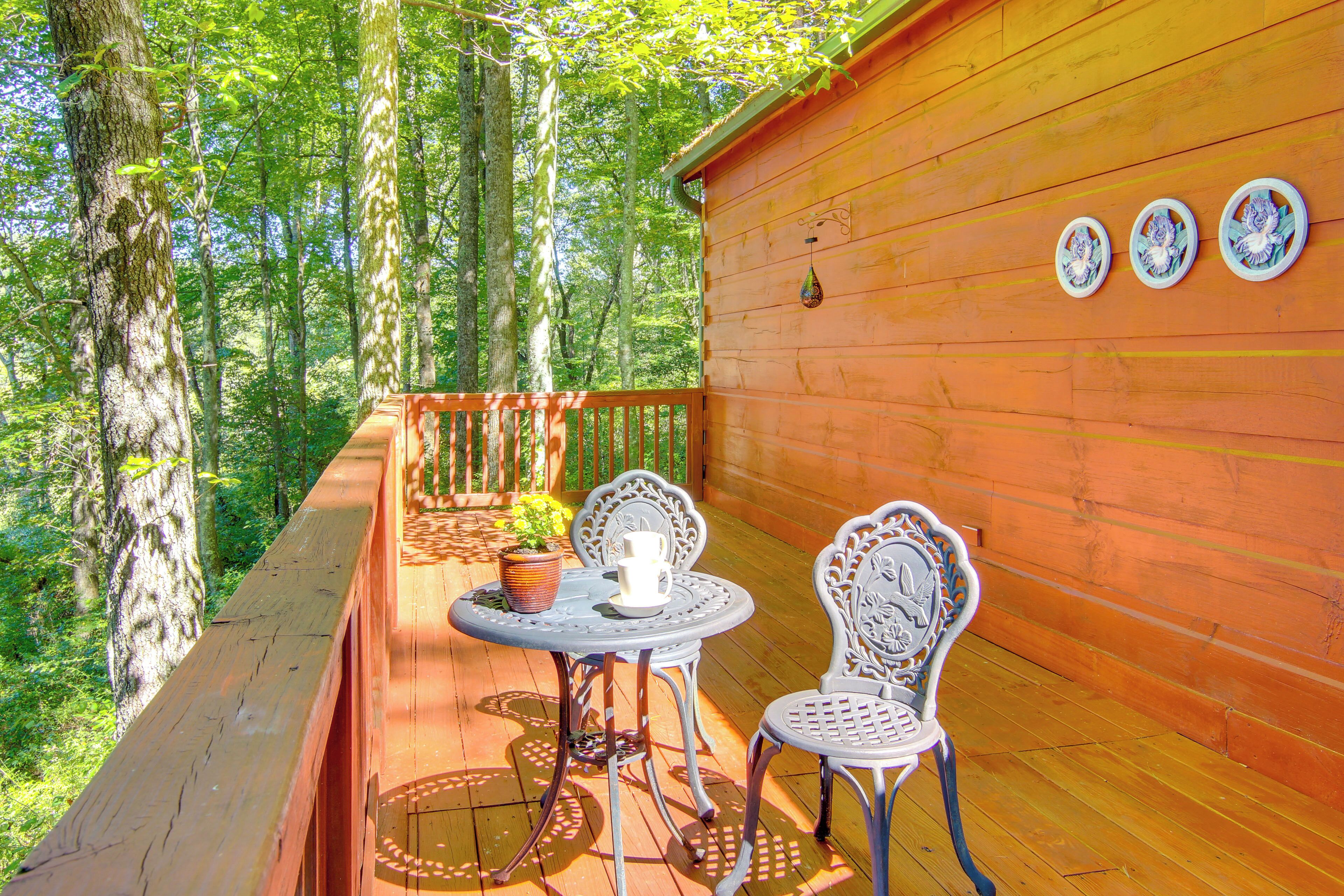 A wooden deck with two ornate metal chairs and a table, surrounded by trees.