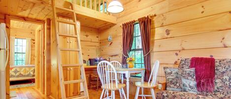 A wooden cabin interior with a dining area, a sofa, and a ladder.