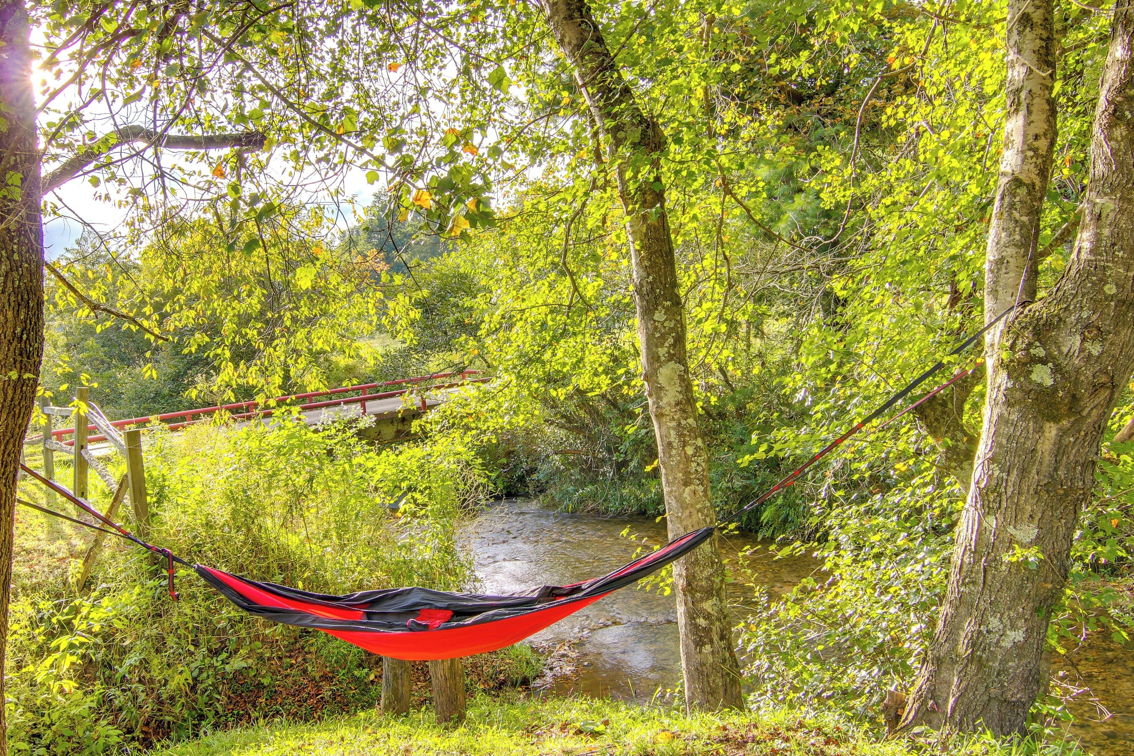 A hammock in a forested area with a bridge in the background.