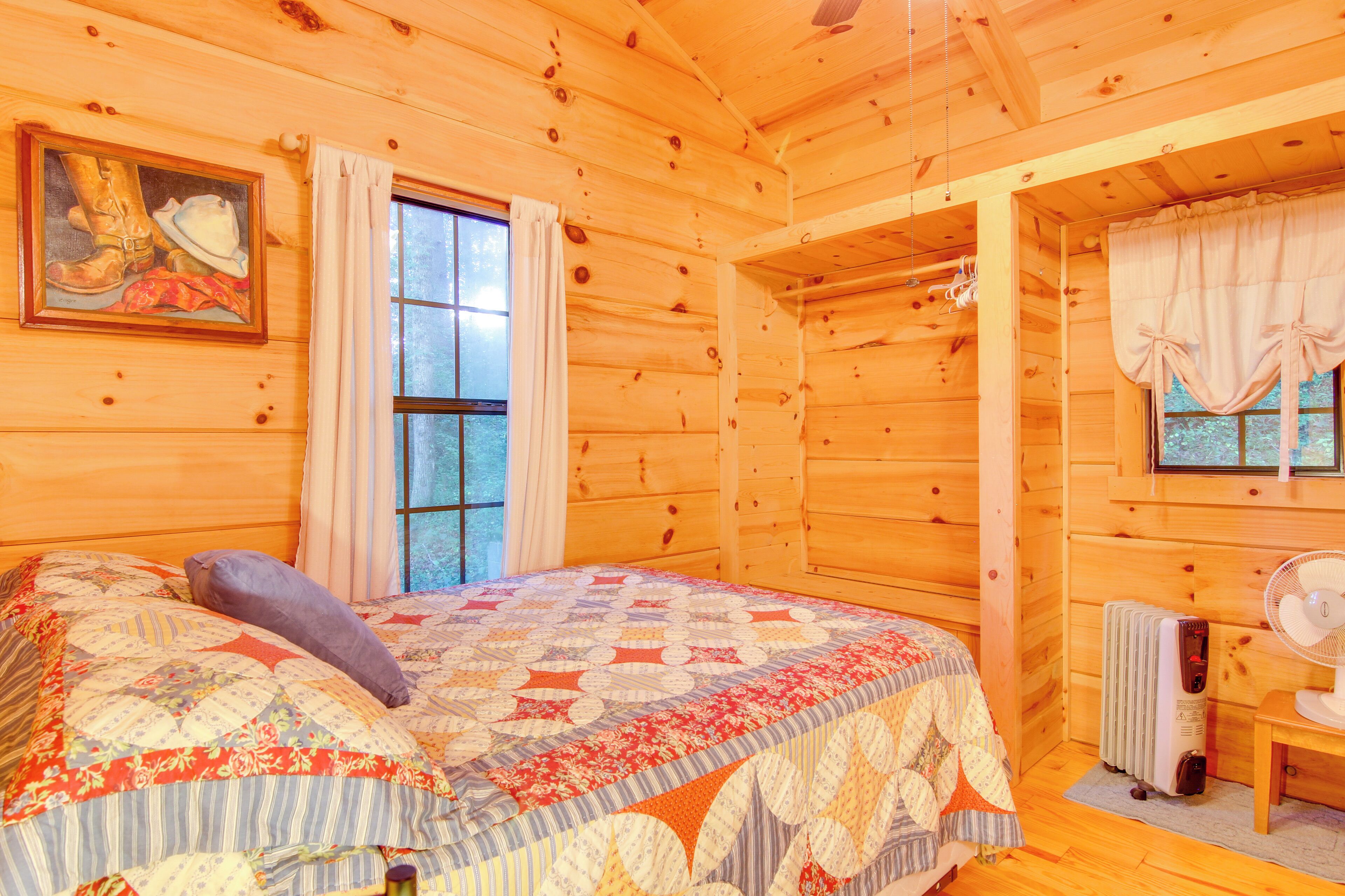 Une pièce de cabane en bois comprenant un lit, une fenêtre, un radiateur et un ventilateur.