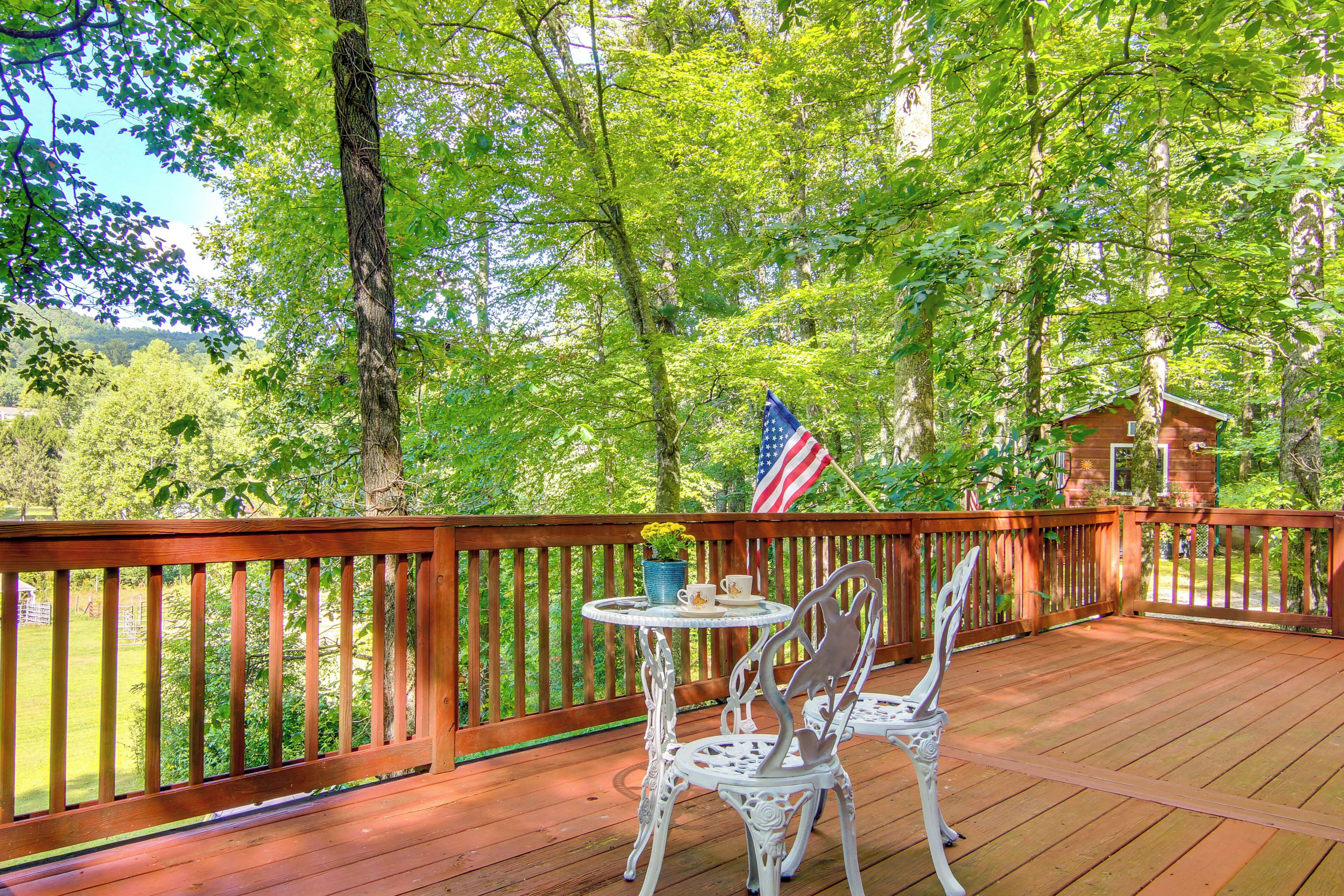 A wooden deck with a table and chairs, surrounded by trees and a view of a house.