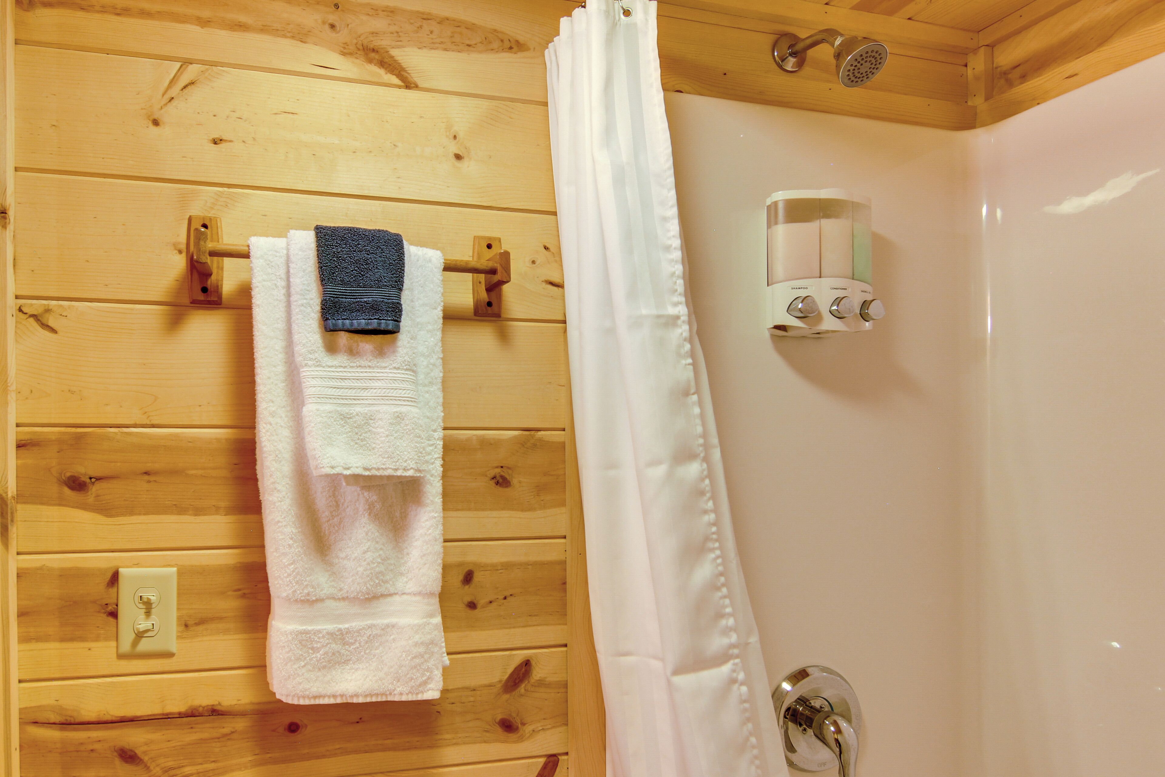 A wooden cabin bathroom with a shower, a towel rack, and a soap dispenser.