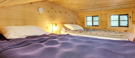 A wooden cabin room with a bed, two windows, and a wall-mounted light fixture.