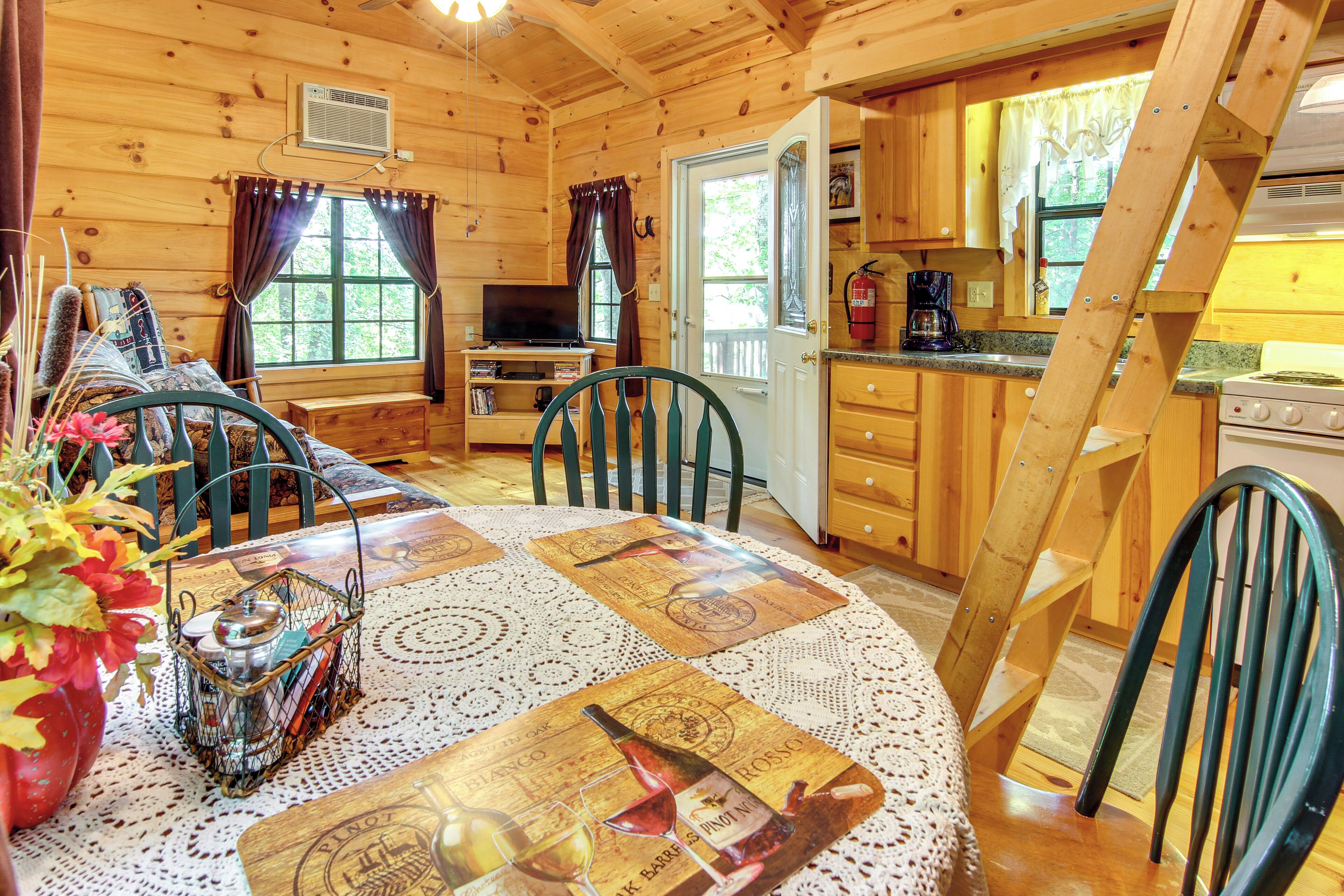 A cozy cabin interior with a dining area, kitchen, and a loft bedroom.