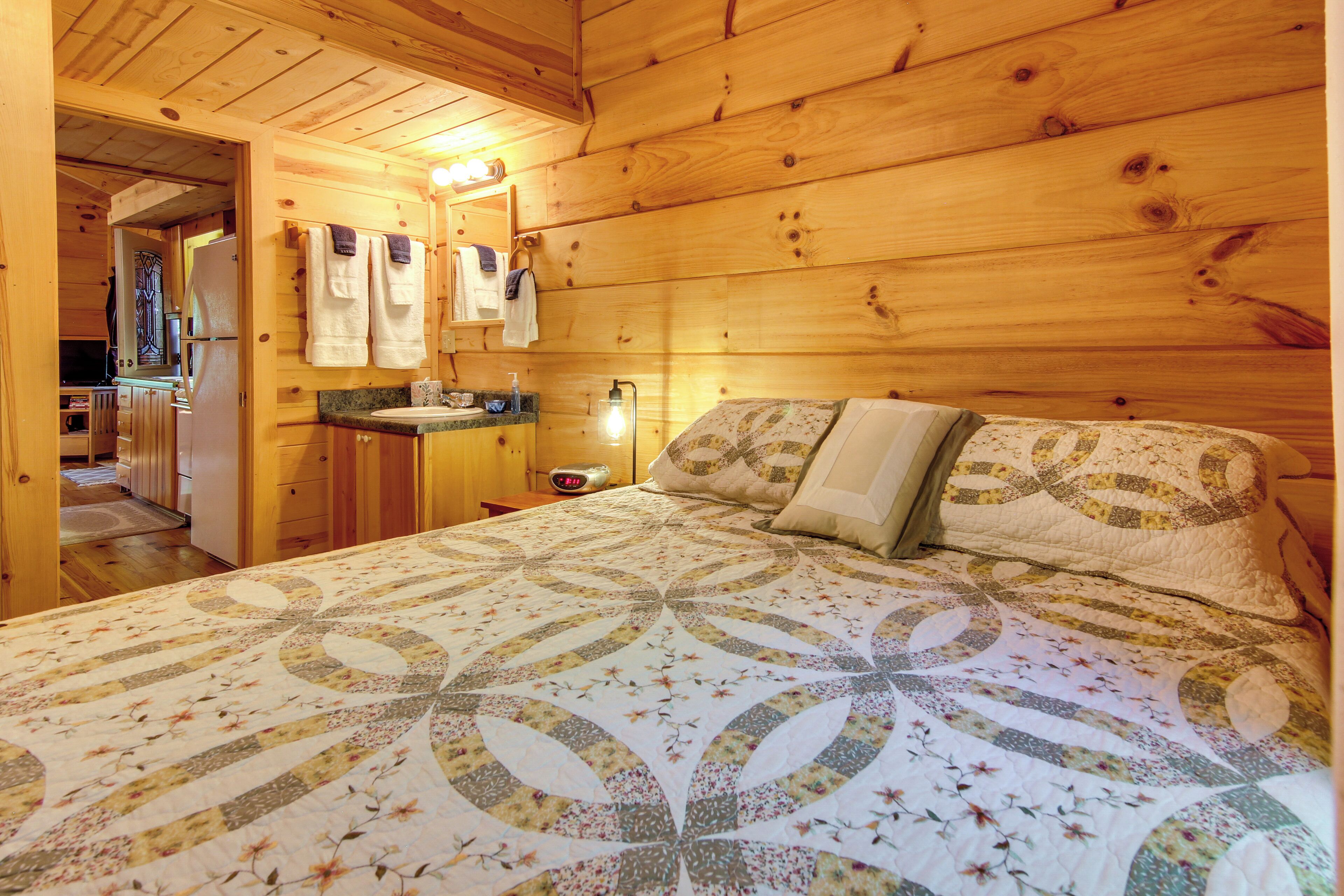 Une chambre à coucher dans une cabane en bois, avec un lit, une table de chevet, un miroir et une salle de bain visible à travers une porte ouverte.