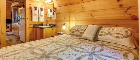 Une chambre à coucher dans une cabane en bois, avec un lit, une table de chevet, un miroir et une salle de bain visible à travers une porte ouverte.