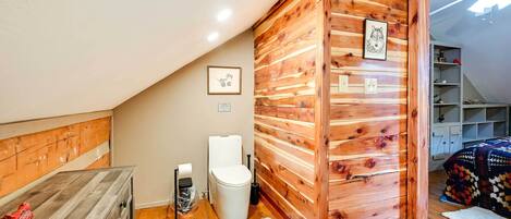 Una habitación pequeña y acogedora con paredes de madera, un inodoro blanco y un armario de madera.