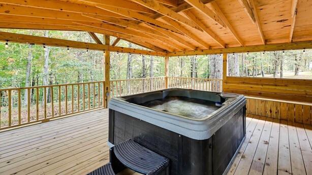 A wooden deck with a hot tub and seating area, surrounded by trees.