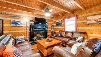 A cozy cabin interior with a fireplace, leather furniture, wooden walls, and various wall decorations.