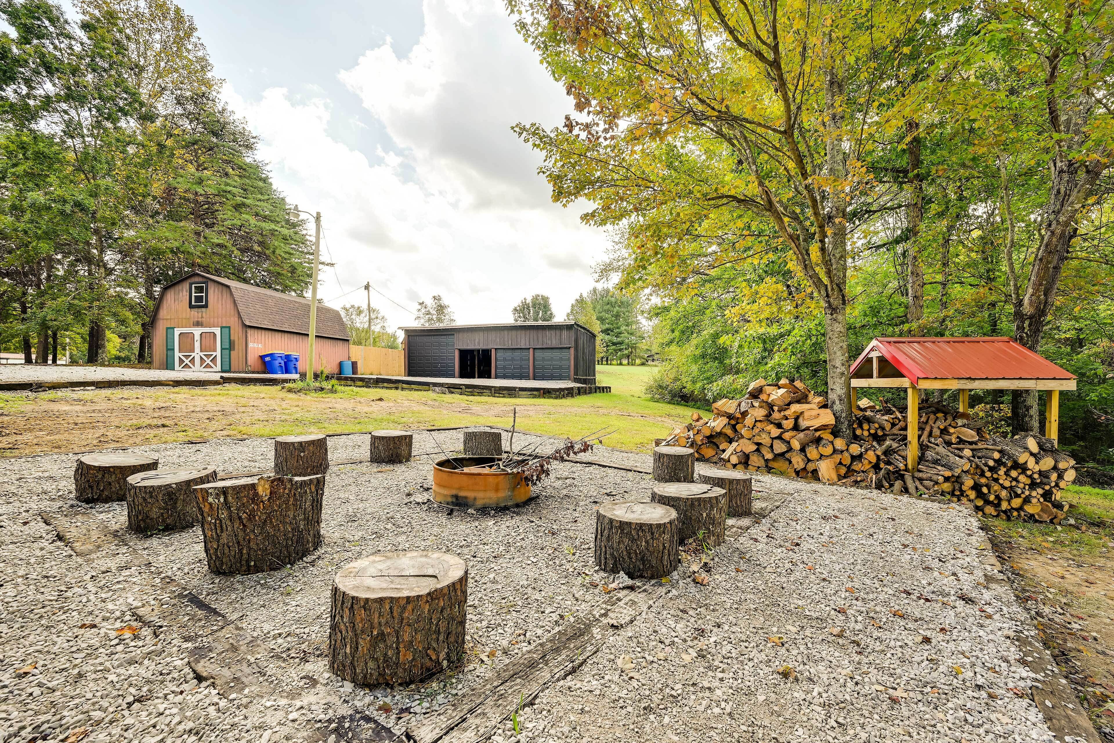 A rustic outdoor seating area with a fire pit, surrounded by wooden stumps and a pile of logs.