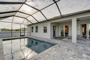 Uma área de piscina coberta ao ar livre, com piso de tijolo, portas de vidro que dão para um pátio e vista do céu.
