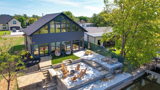 Ein modernes Haus mit einer großen Glasfassade, einer Terrasse mit Gartenmöbeln und einem kleinen Wasserspiel.