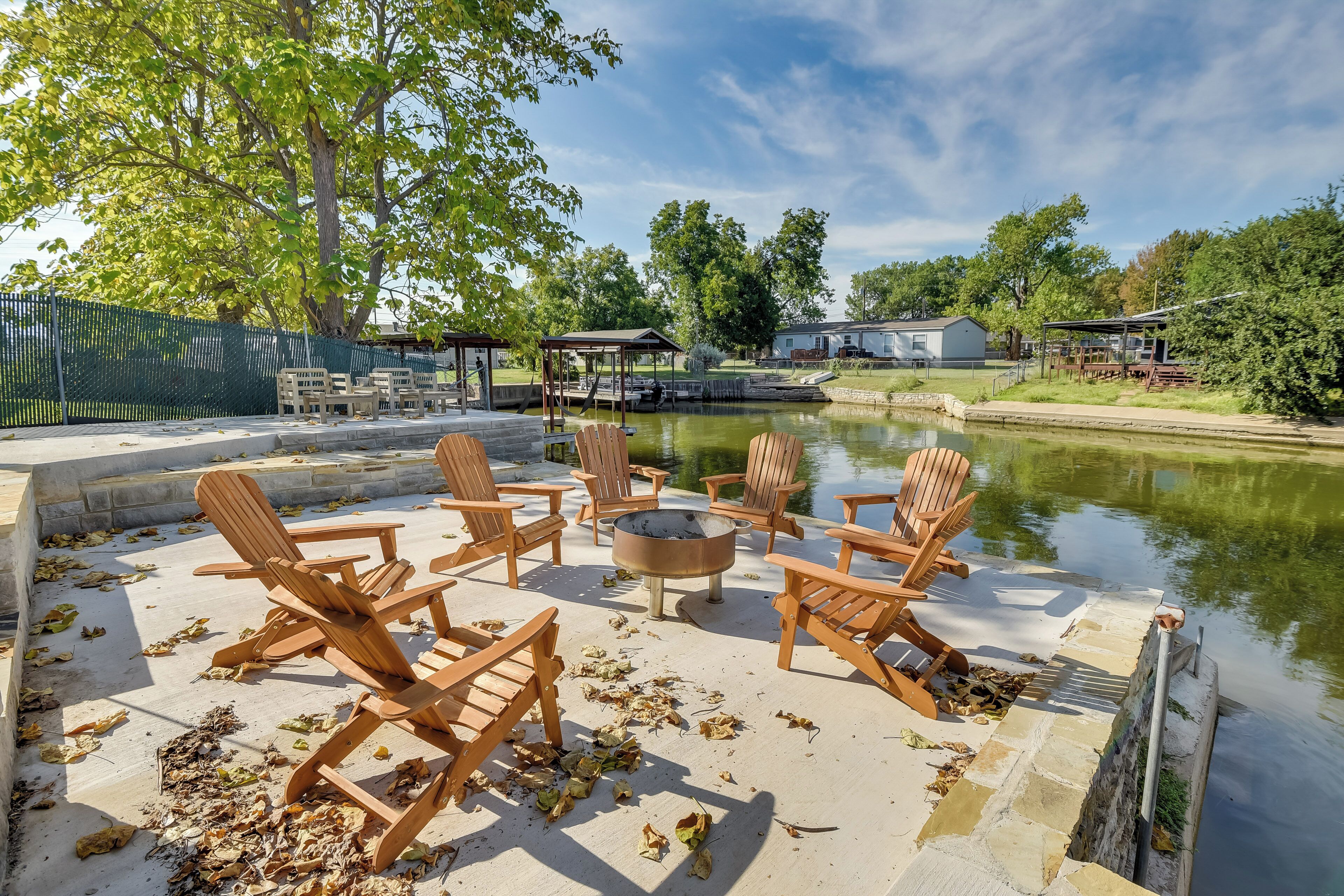 An outdoor seating area with wooden chairs and a fire pit, overlooking a calm water body.