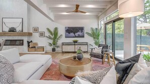 Ein modernes Wohnzimmer mit einem weißen Sofa, einem runden Couchtisch und einem großen Fenster mit Blick ins Freie.