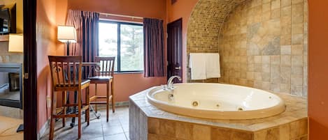 A bathroom with a large bathtub, wooden chairs, a window with curtains, and a tiled wall.