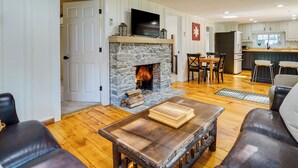 A living room with a stone fireplace, wooden flooring, a television on the mantel, and leather furniture. - 'mount Pine' Winter Retreat Near the Green Mtns! (Wardsboro)