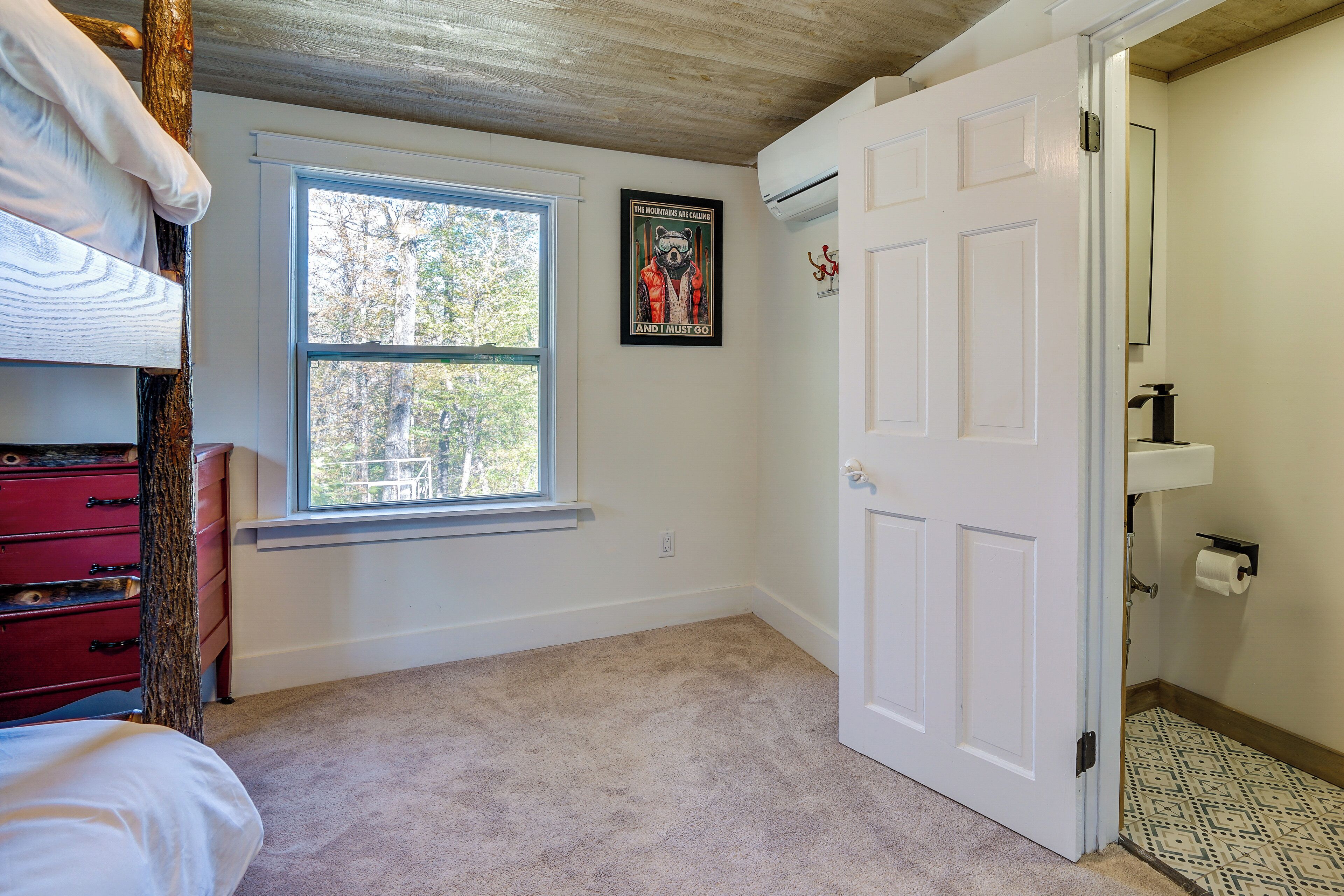 A bedroom with a bunk bed, a window, a door, and a poster on the wall.