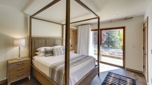 Een hemelbed met houten frame, een nachtkastje met lades, en uitzicht op een tuin via een glazen deur.