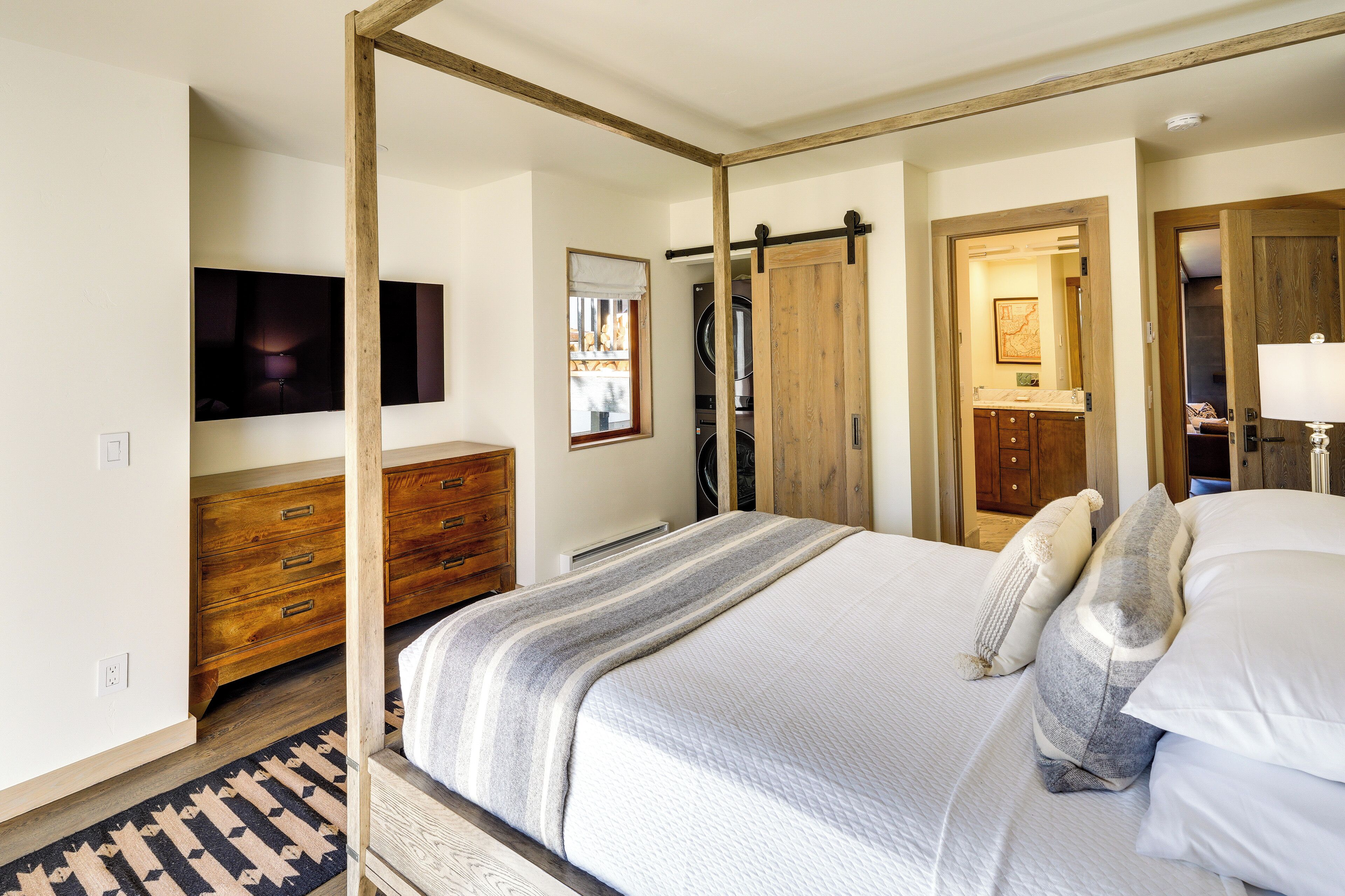 A bedroom with a bed, wooden dresser, and a TV mounted on the wall.