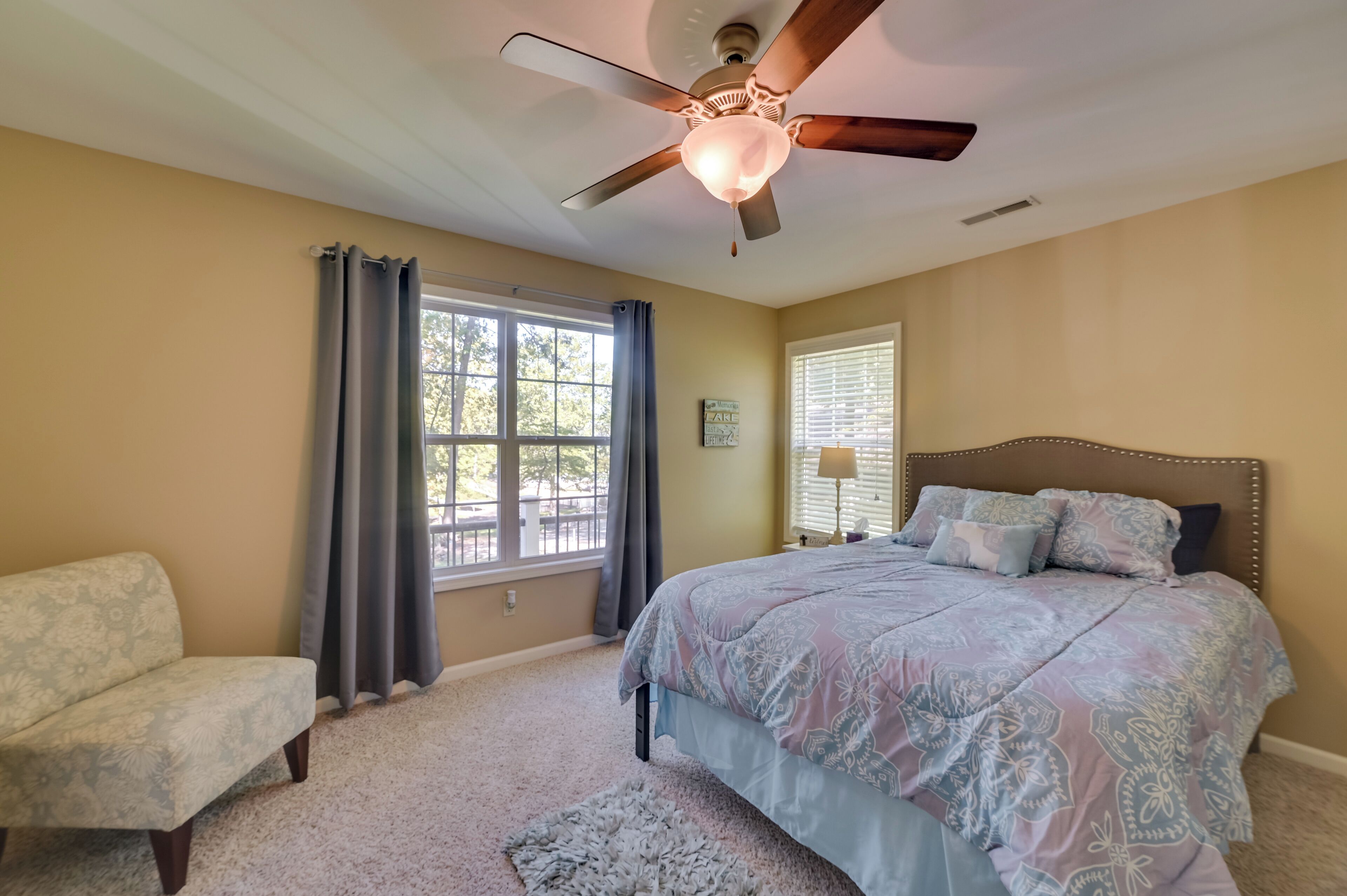 A bedroom with a large bed, a ceiling fan, a window with curtains, and a chair.