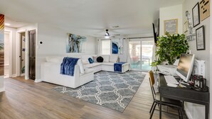 A modern living room with a white sectional sofa, a desk with a computer, and a large plant.