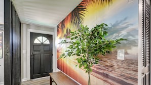 A hallway with a wooden bench, a door, and a large tropical mural on the wall.