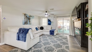 A modern living room with a white sectional sofa, a ceiling fan, and artwork on the walls.