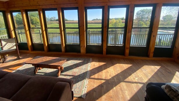 A spacious room with large windows offering views of a lake and surrounding greenery.