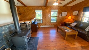A cozy cabin interior with a stone fireplace, wooden walls, a leather sofa, and a ceiling fan.
