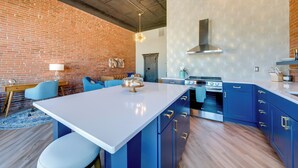 Een moderne keuken met blauwe kastjes, een wit eiland en een bakstenen muur.
