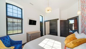 Een slaapkamer met een groot bed, een dressoir, een televisie en een raam met jaloezieën.