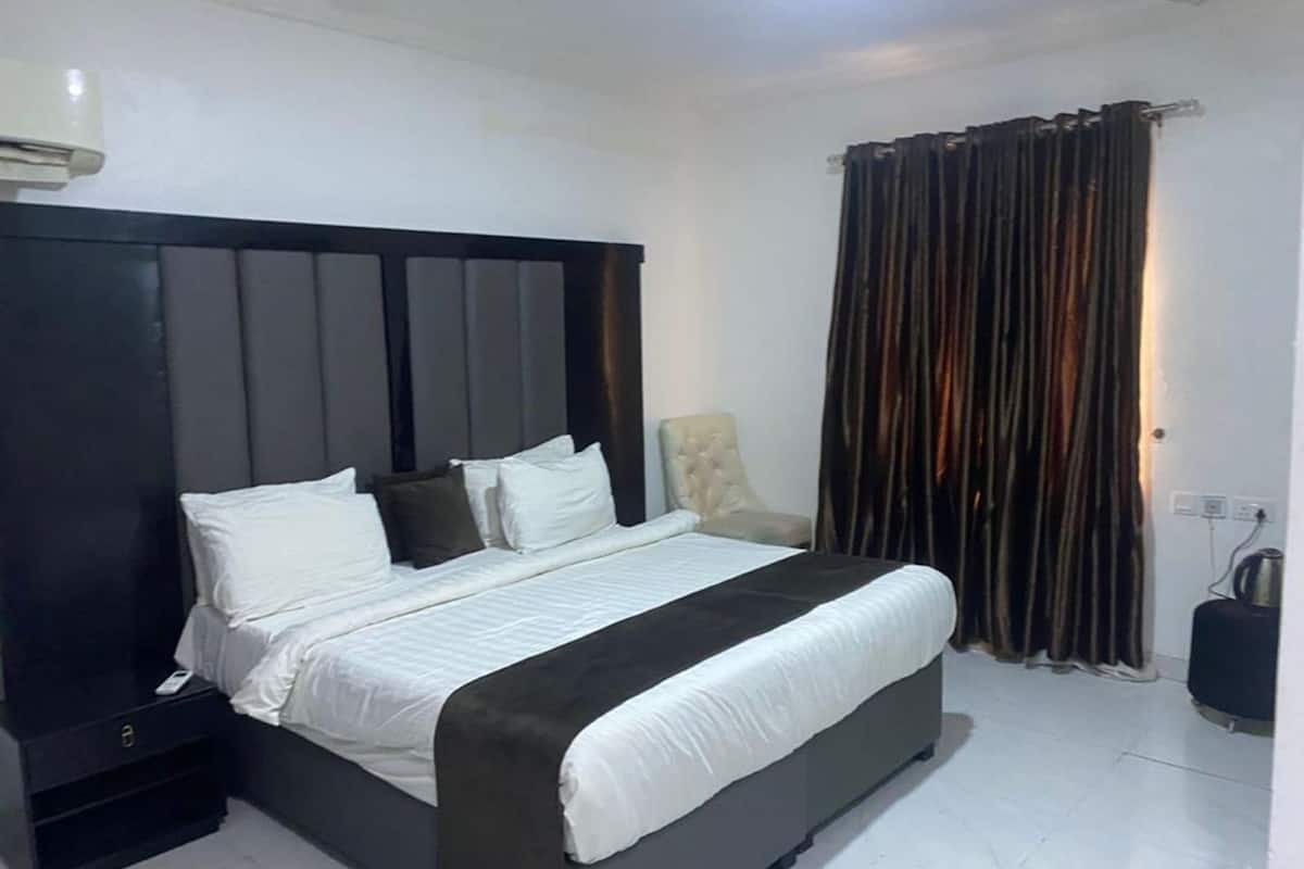 A bedroom with a large bed, a chair, a curtain, and a kettle.