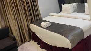 Une chambre d’hôtel avec un lit, une chaise, un rideau et un luminaire au plafond.