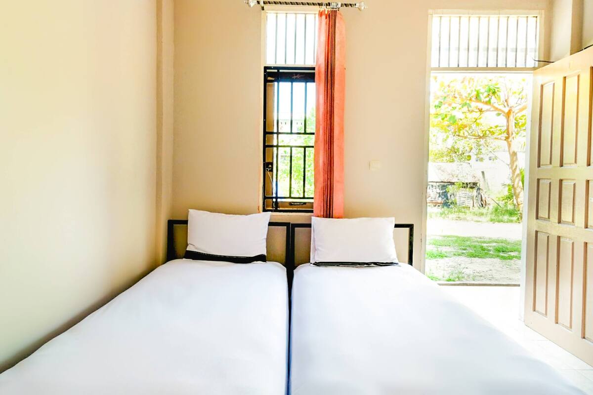 A room with two beds, a window with bars, and a view of the outside.
